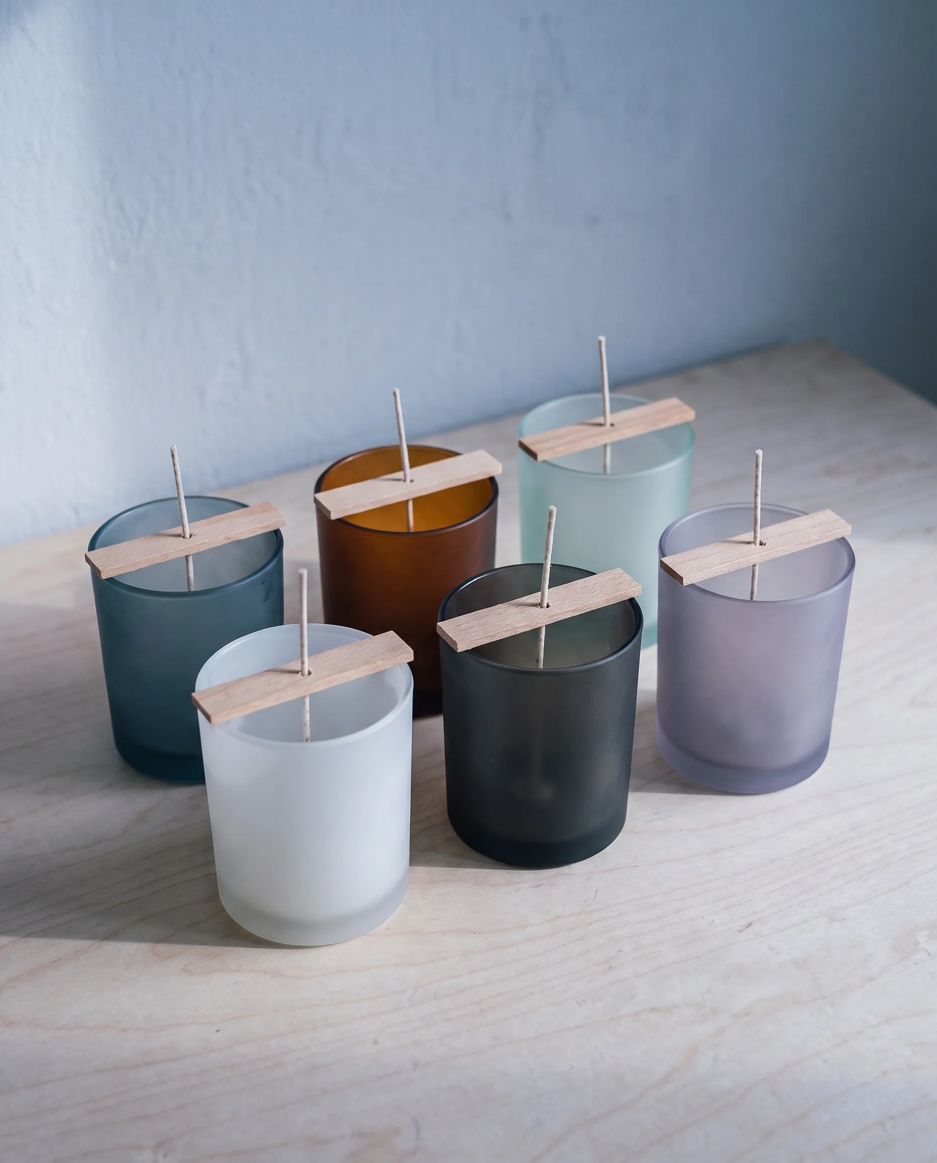 Cotton wicks held upright and centred in empty frosted glass tumblers on the workbench, ready for pouring.